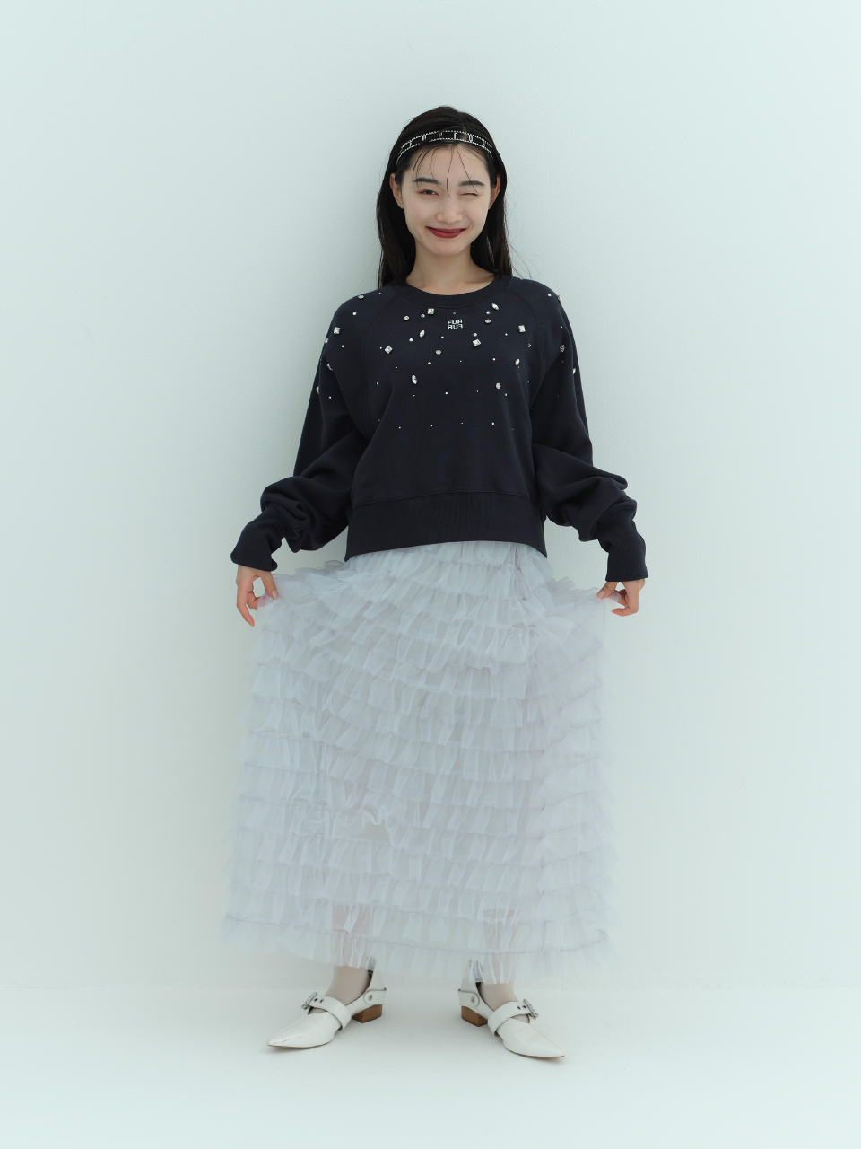 ビジュー付きロゴ刺繍スウェット・チュールフリルティアードスカート・ロゴクリスタルカチューシャ・【WEB限定カラー】ダブルストラップバブーシュを着用した女性