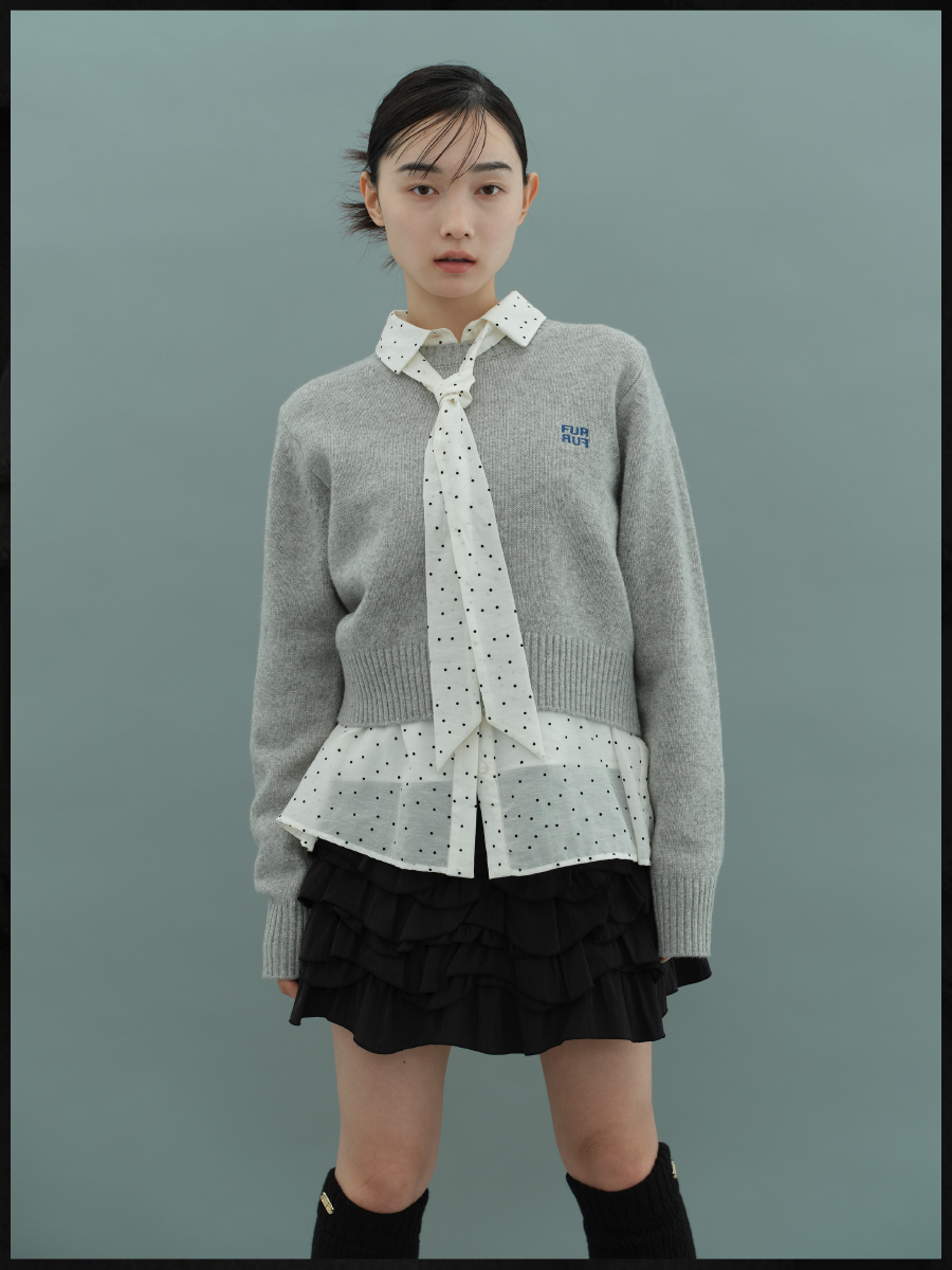 ネクタイセットブラウス・ロゴ刺繍クルーネックセーター・フリルティアードミニスカート・【限定カラー】エコファーマーケットバッグ・レッグウォーマーを着用した女性