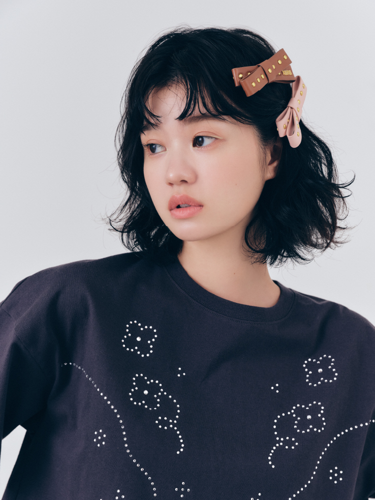 ビジューデザインＴシャツ・レザーライクミディスカート・スタッズリボンヘアクリップを着用した女性