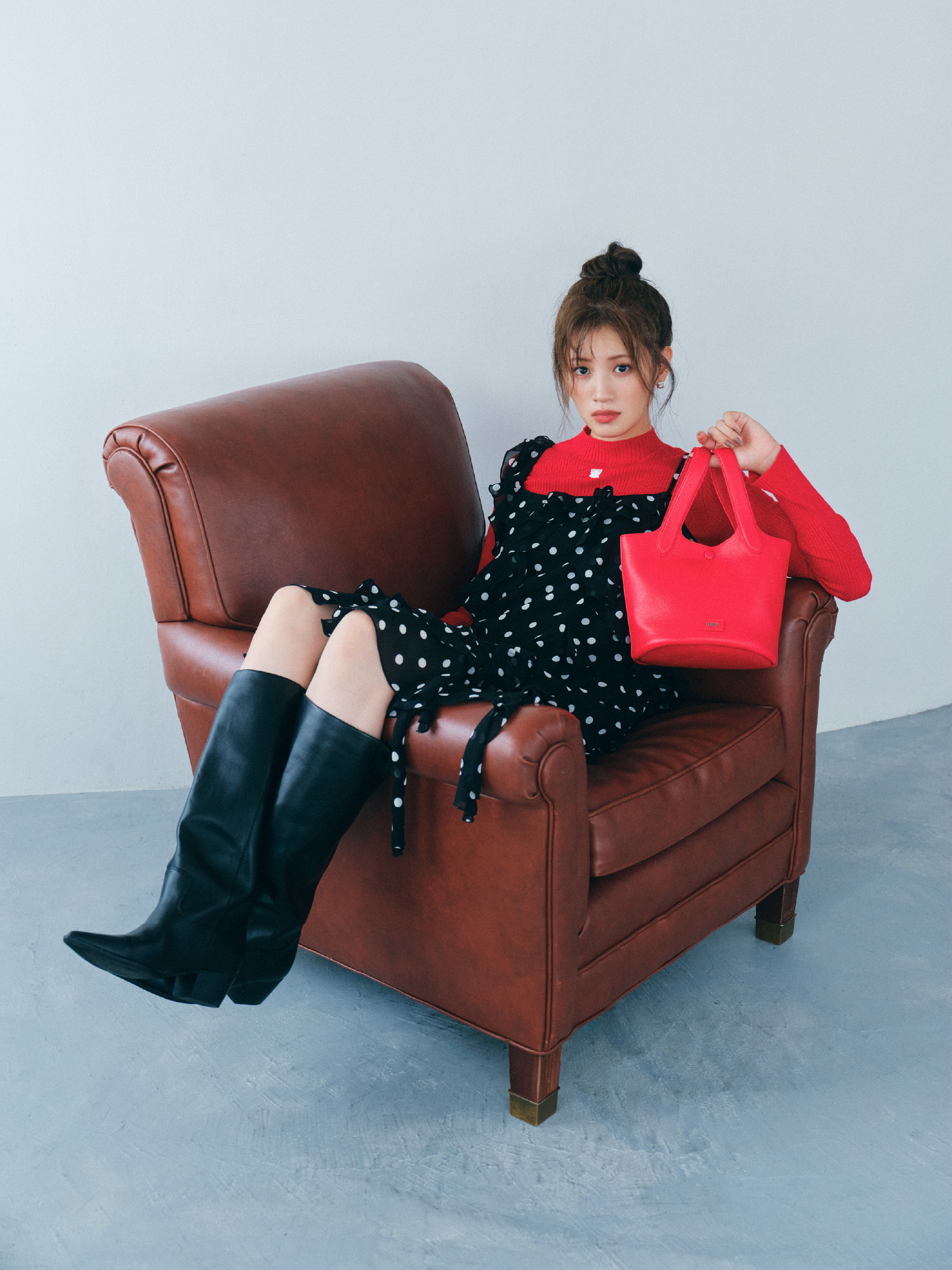 【限定カラー】リボン刺繍リブニットトップス・フリルキャミソールワンピース・リボンピアス・【WEB限定カラー】ロゴカシメバケットバッグ・ウエスタンロングブーツを着用した女性