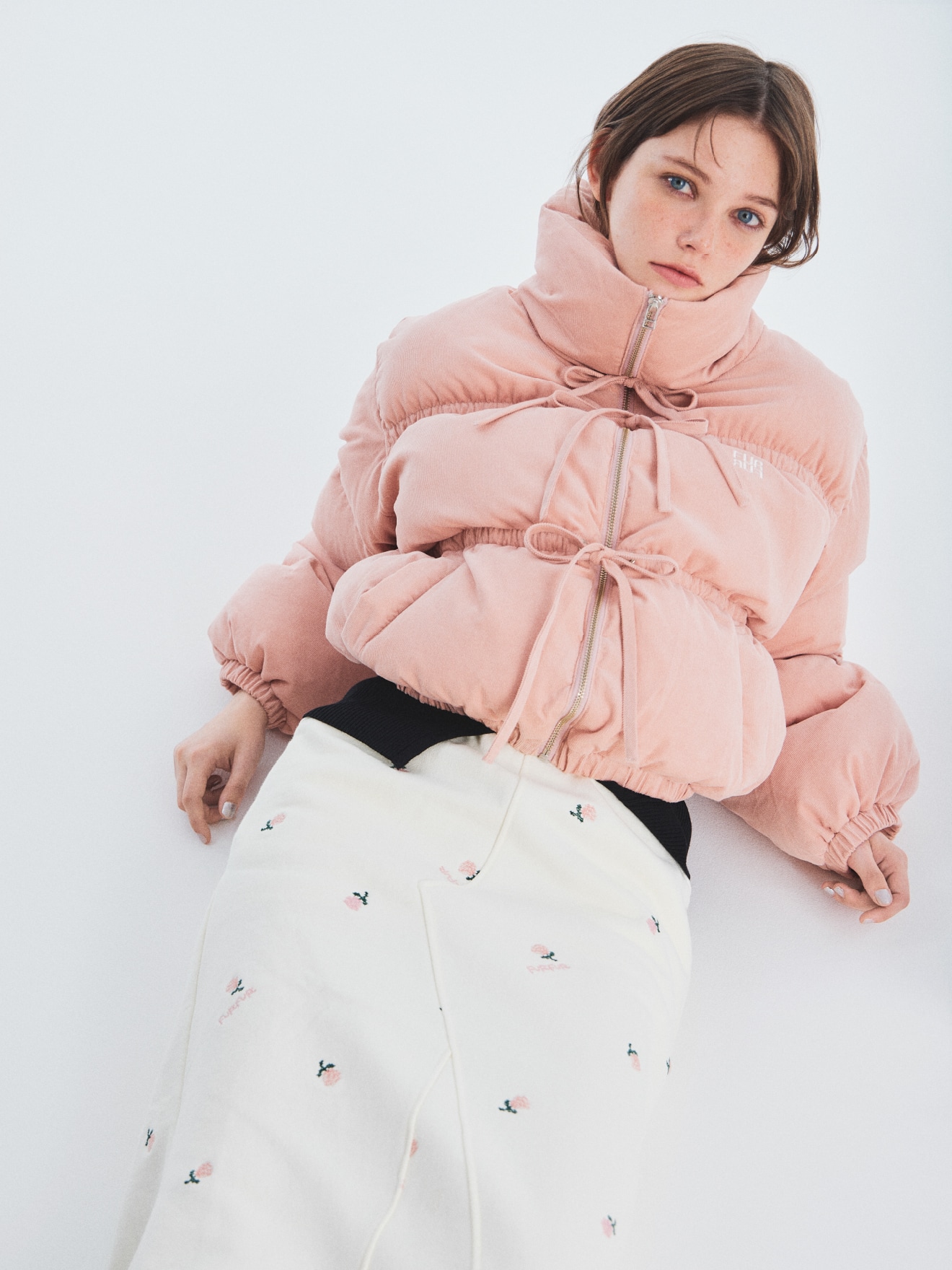 ピンクのリボンショートダウンジャケット、ブラックのスラッシュデザインニットビスチェ、アイボリーのフラワー刺繍スウェットスカート、ピンクのパールチロリアンシューズのコーディネート例