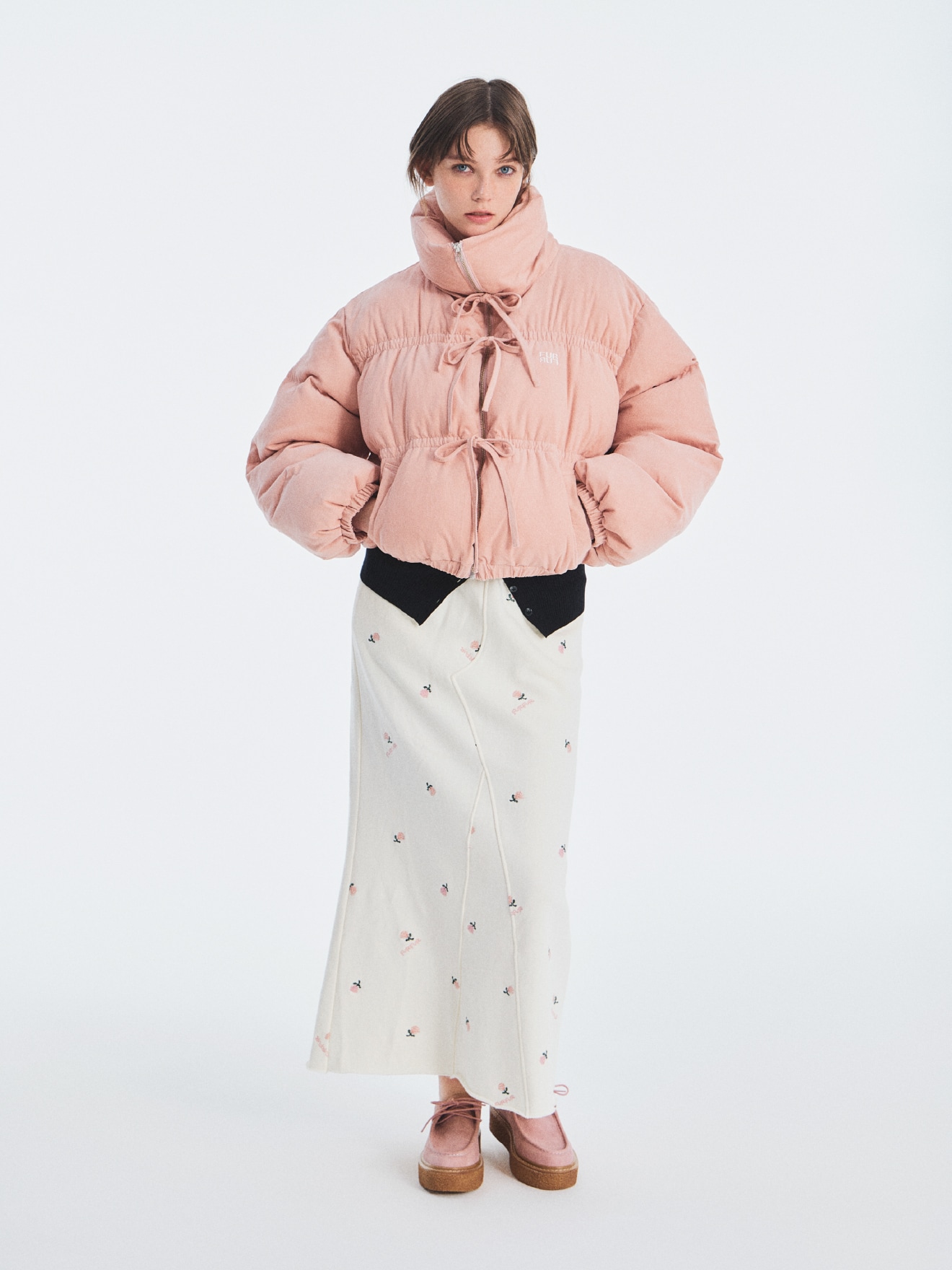 ピンクのリボンショートダウンジャケット、ブラックのスラッシュデザインニットビスチェ、アイボリーのフラワー刺繍スウェットスカート、ピンクのパールチロリアンシューズのコーディネート例