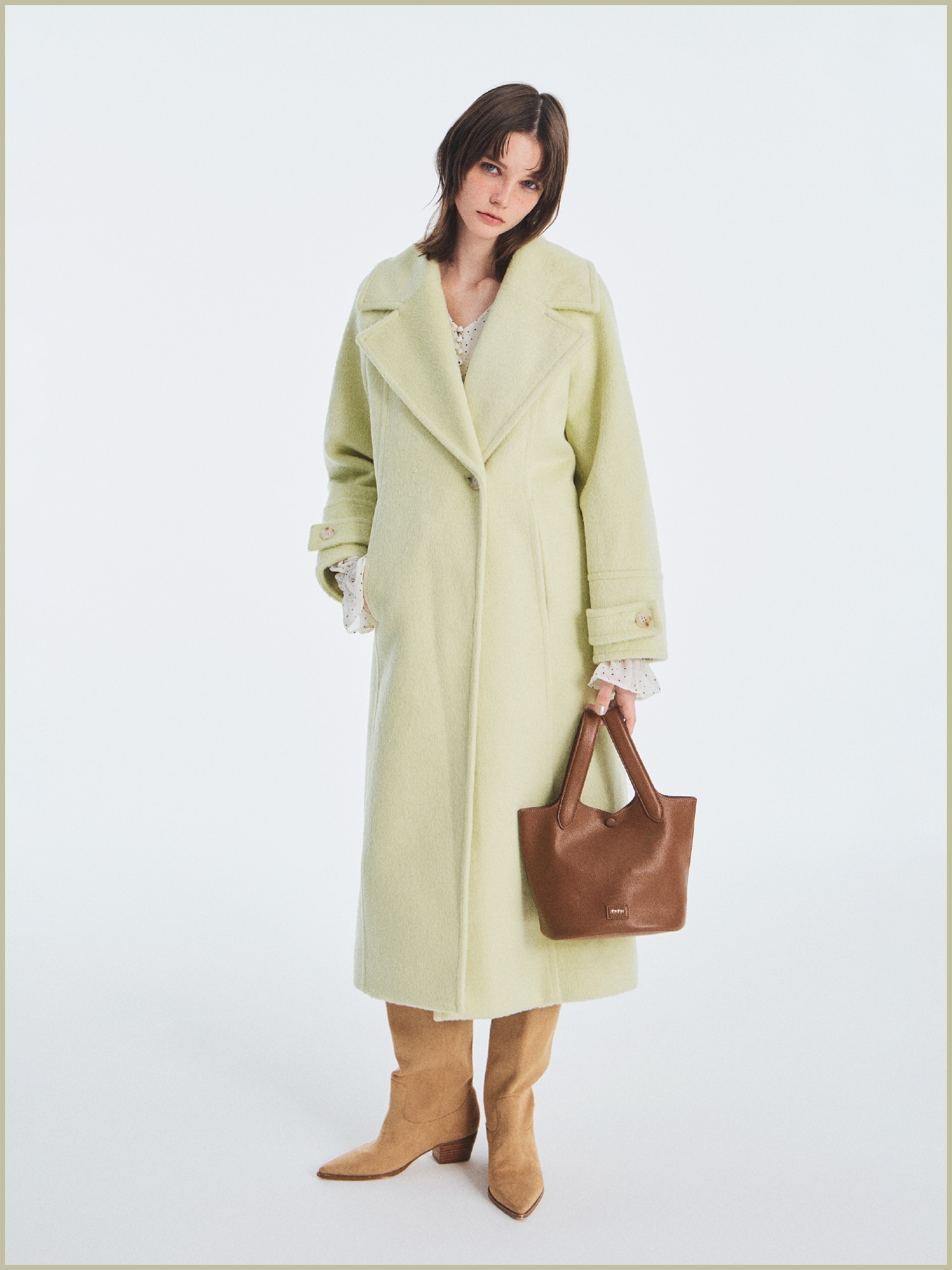 ライム色のシャギーロングコート、オフホワイトのフリルチュニックブラウス、チェック柄のクロスベルトショートパンツ、ロゴカシメバケットバッグ、ウエスタンロングブーツのコーディネート例