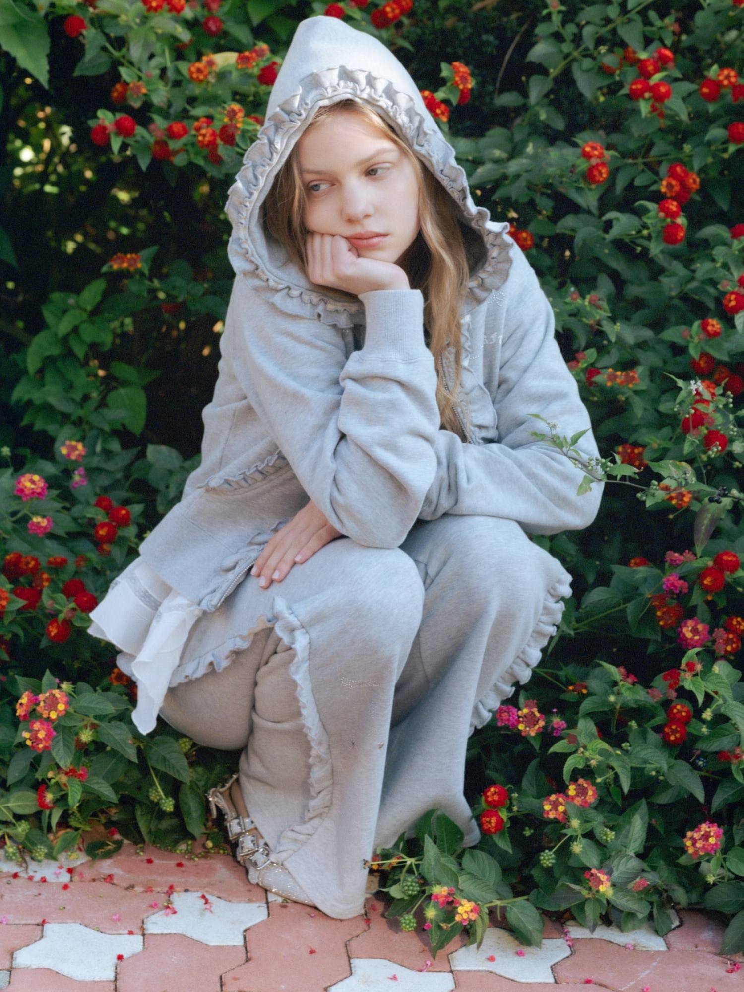 グレーのフリルジップアップフーディー・グレーのフリルスウェットパンツ・黒のフラワー刺繍ケーブルカーディガン・白のハンカチ刺繍チュニックブラウス・シルバーのクロスストラップアイレットシューズを合わせたコーディネート