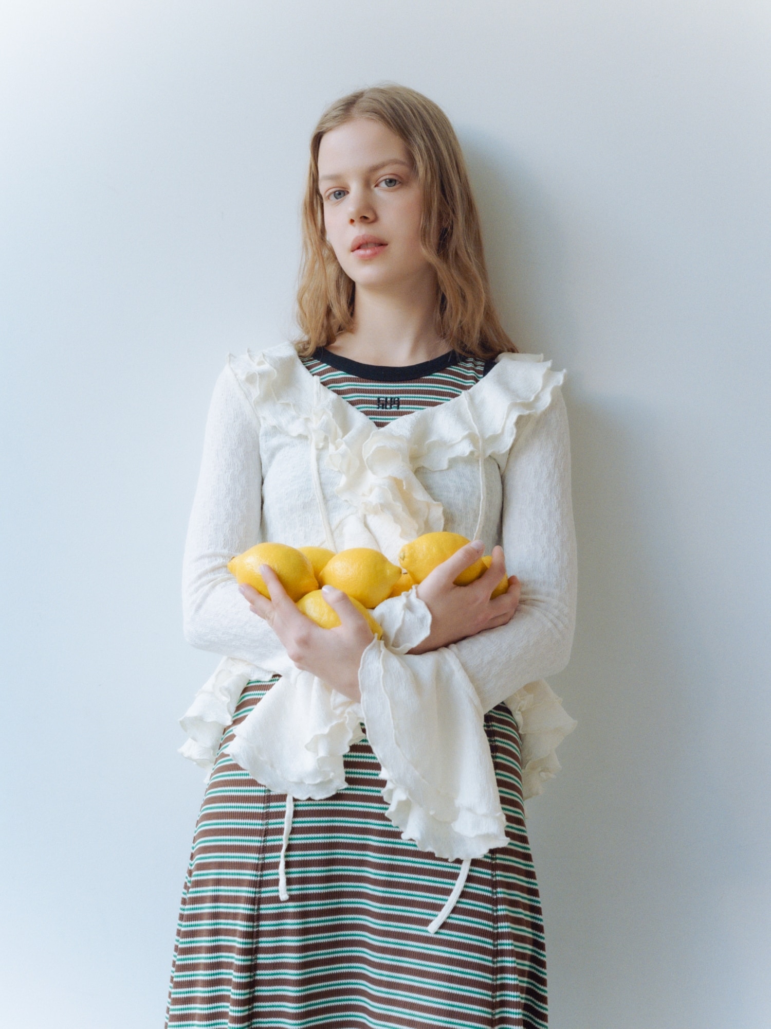 ブラウンのロゴ刺繍ボーダーワンピース・アイボリーのラッフルフリルプルオーバー・ゴールドのハートモチーフイヤリング・ブラウンのミニリボンカシメローファーを合わせたコーディネート