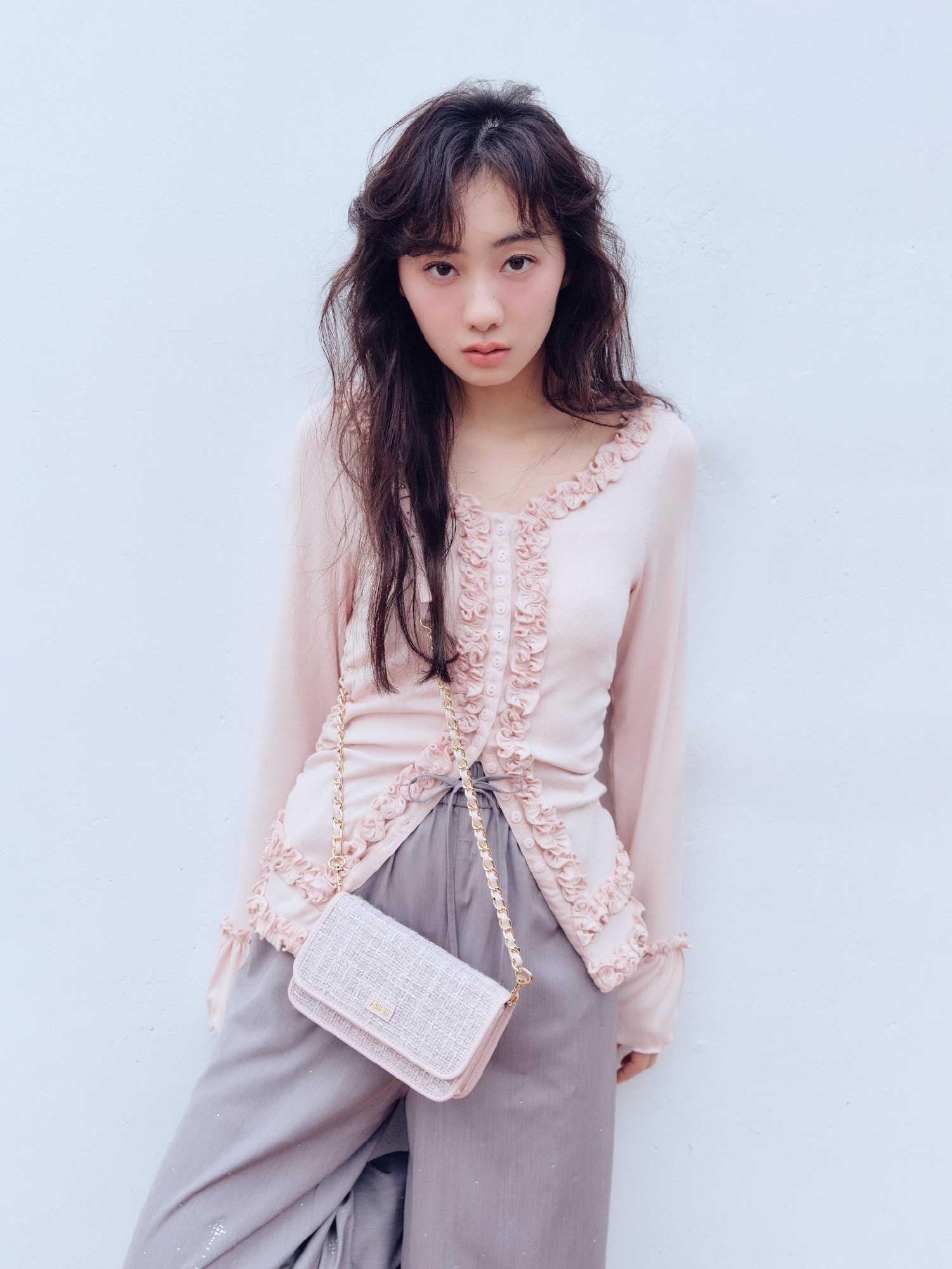 ピンクのフリルカーディガン・ピンクのトリミング刺繍レザーライクブルゾン・ライトグレーのビジュー付きイージーパンツ・ピンクのツイードロゴフォンホルダー・シルバーのクロスストラップアイレットシューズを合わせたコーディネート