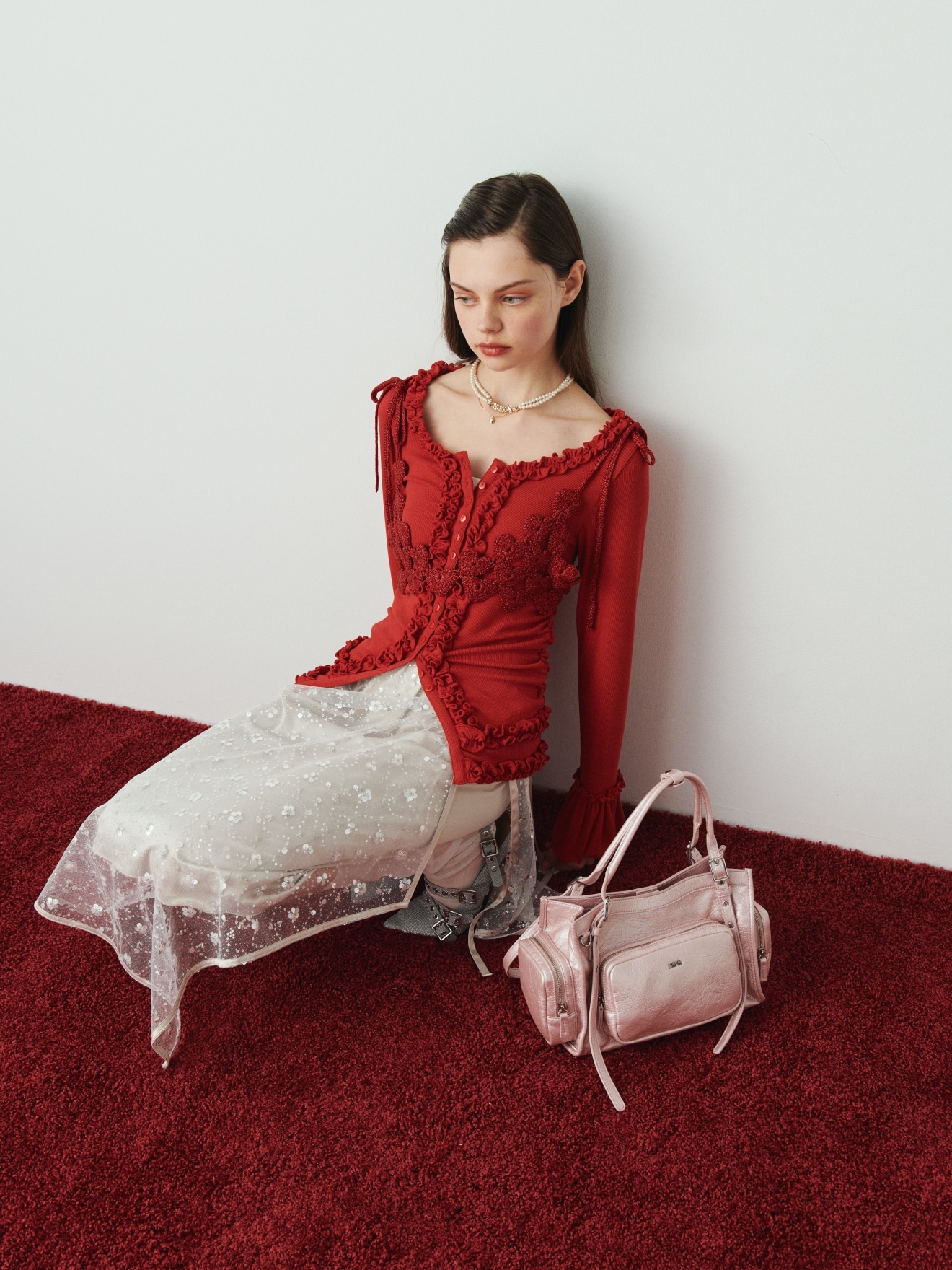 赤のフリルカーディガン・シルバーのスパンコールラップスカート・赤のかぎ針ハートモチーフビスチェ・ピンクのアウトポケットバッグ・ゴールドのフラワーモチーフパールネックレスとハートモチーフネックレス・シルバーのクロスストラップアイレットシューズを合わせた、甘めのディテールが大人可愛いムードを添えるコーディネート