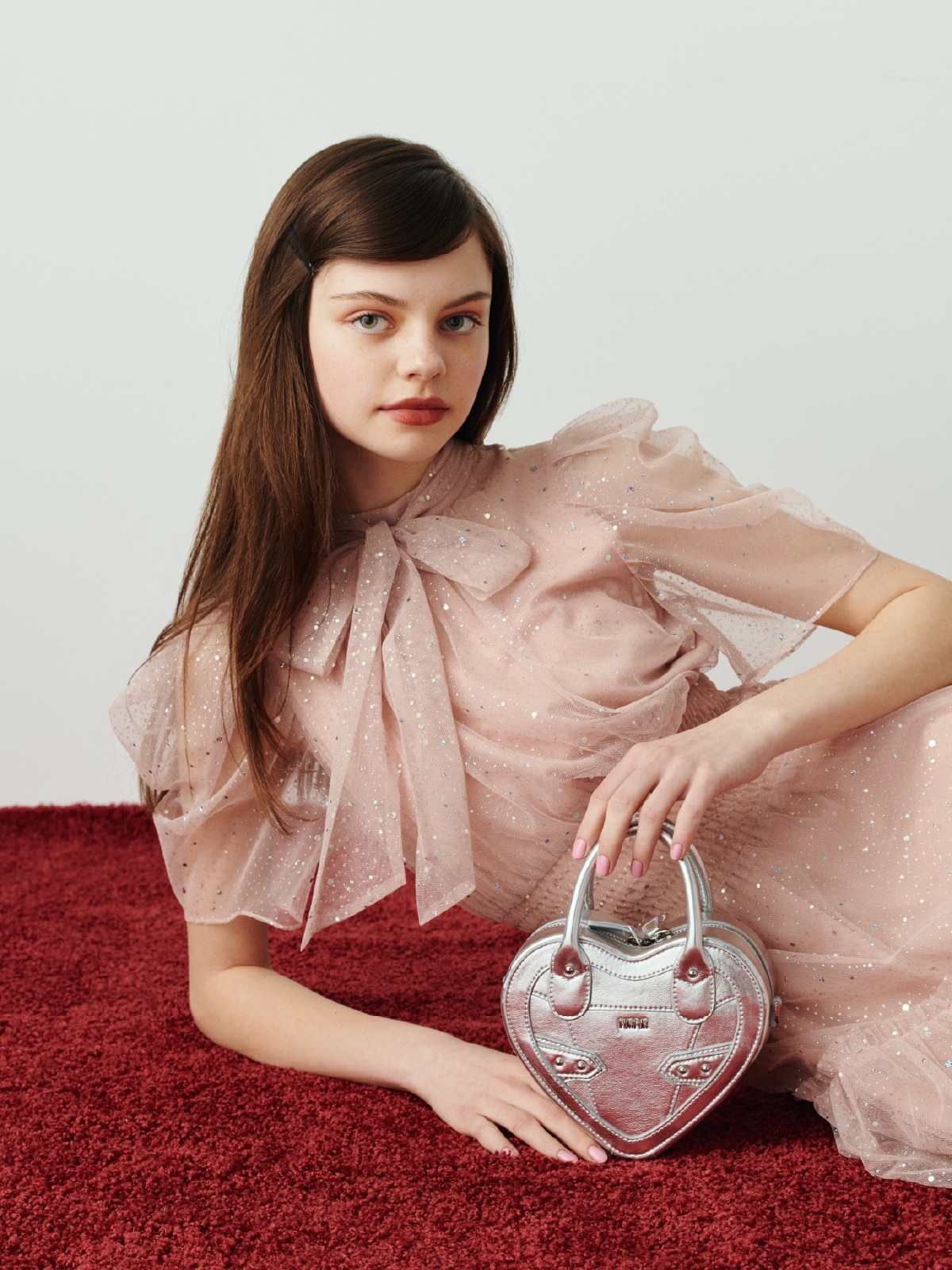 ピンクのハーフスリーブラメチュールドレス・シルバーのハートショルダーバッグを合わせた、繊細な透け感と動きのあるシルエットが女性らしいコーディネート