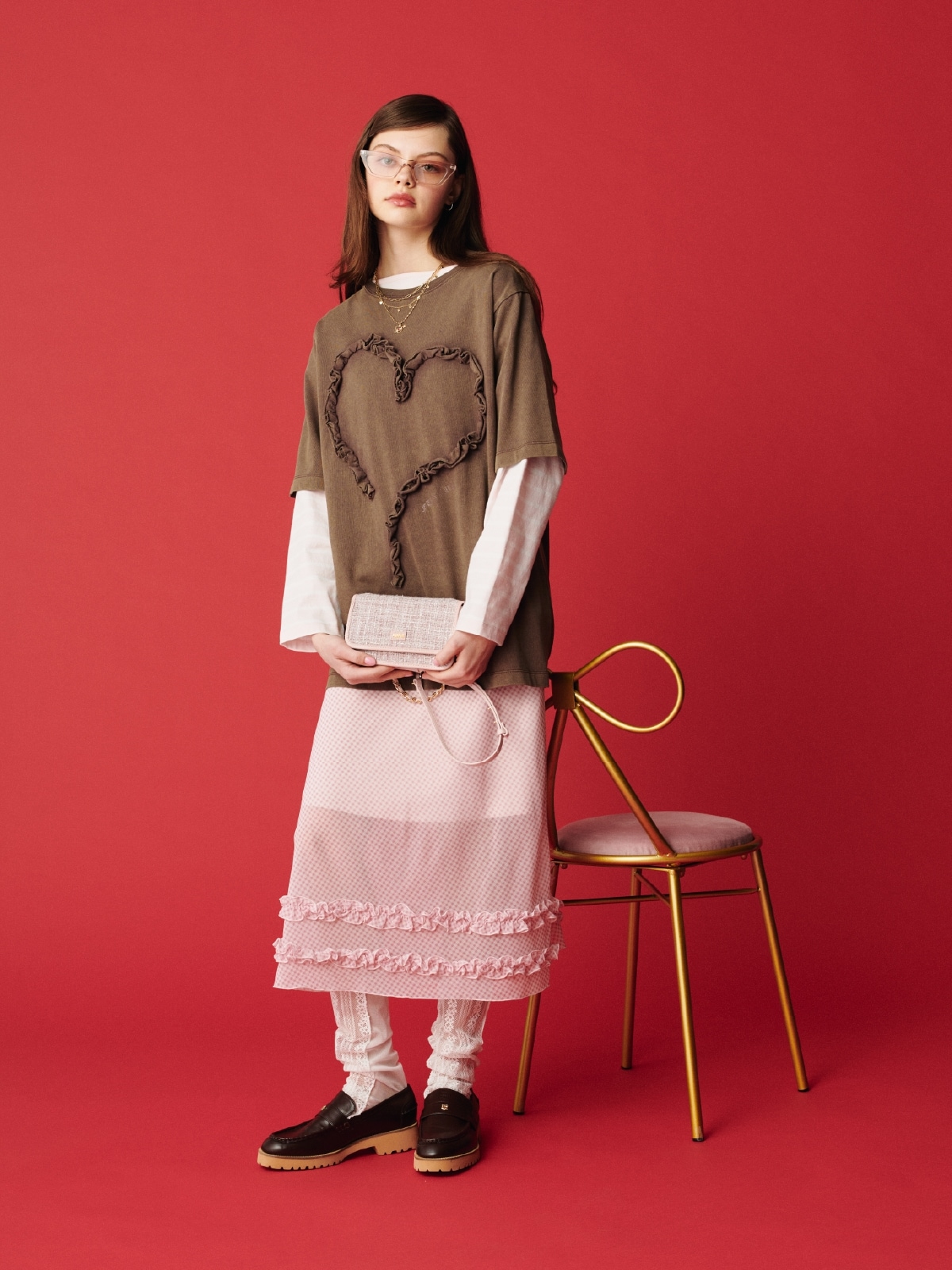 ブラウンのフリルハートモチーフＴシャツ・ピンクのバスクボーダーロングスリーブＴシャツとミディナロースカートとツイードロゴフォンホルダー・ゴールドのハートモチーフ３連ネックレス・ピンクのアイウェア・ブラウンのミニリボンカシメローファーを合わせた、甘めのディテールが大人可愛いムードを添えるコーディネート