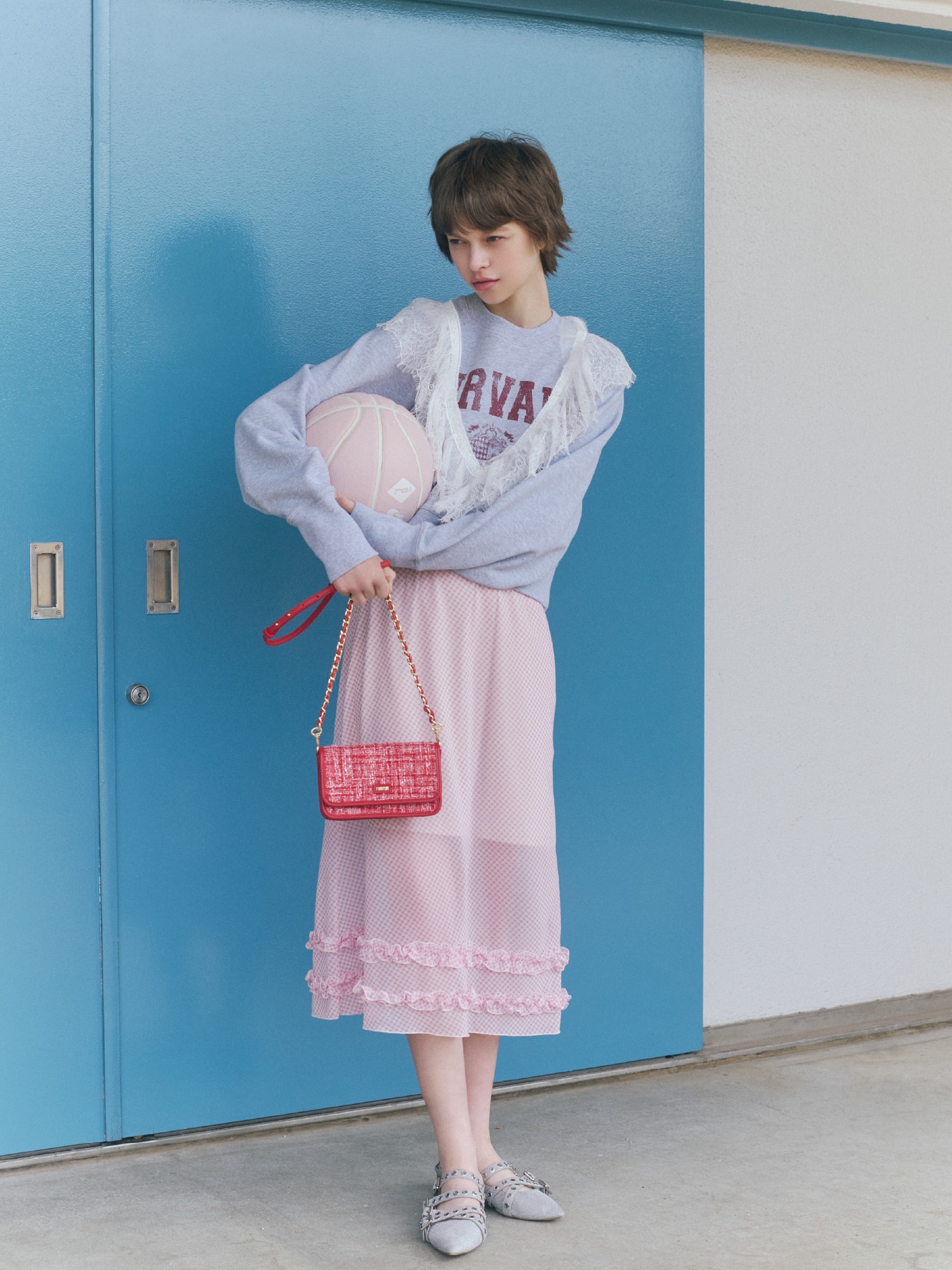 グレーのスウェットシャツにピンクのスカートを合わせ、アクセントにレッドのバッグとシルバーのシューズを取り入れたコーディネート。