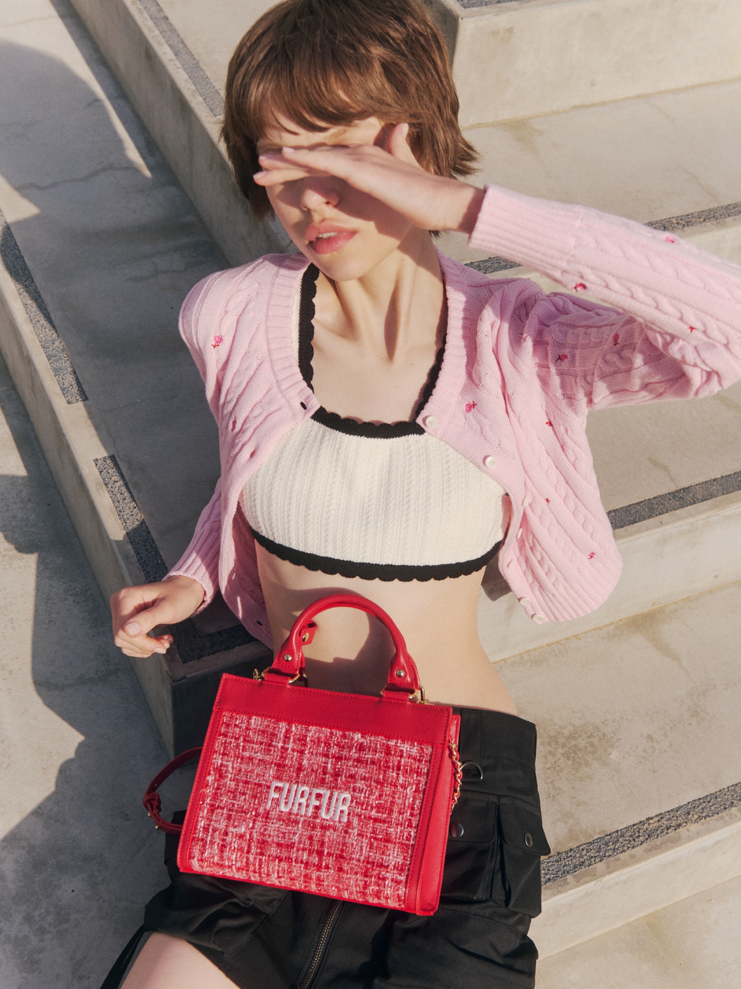 ピンクのカーディガンとピンクのビスチェにブラックのスカートを合わせ、レッドのバッグを取り入れたコーディネート。