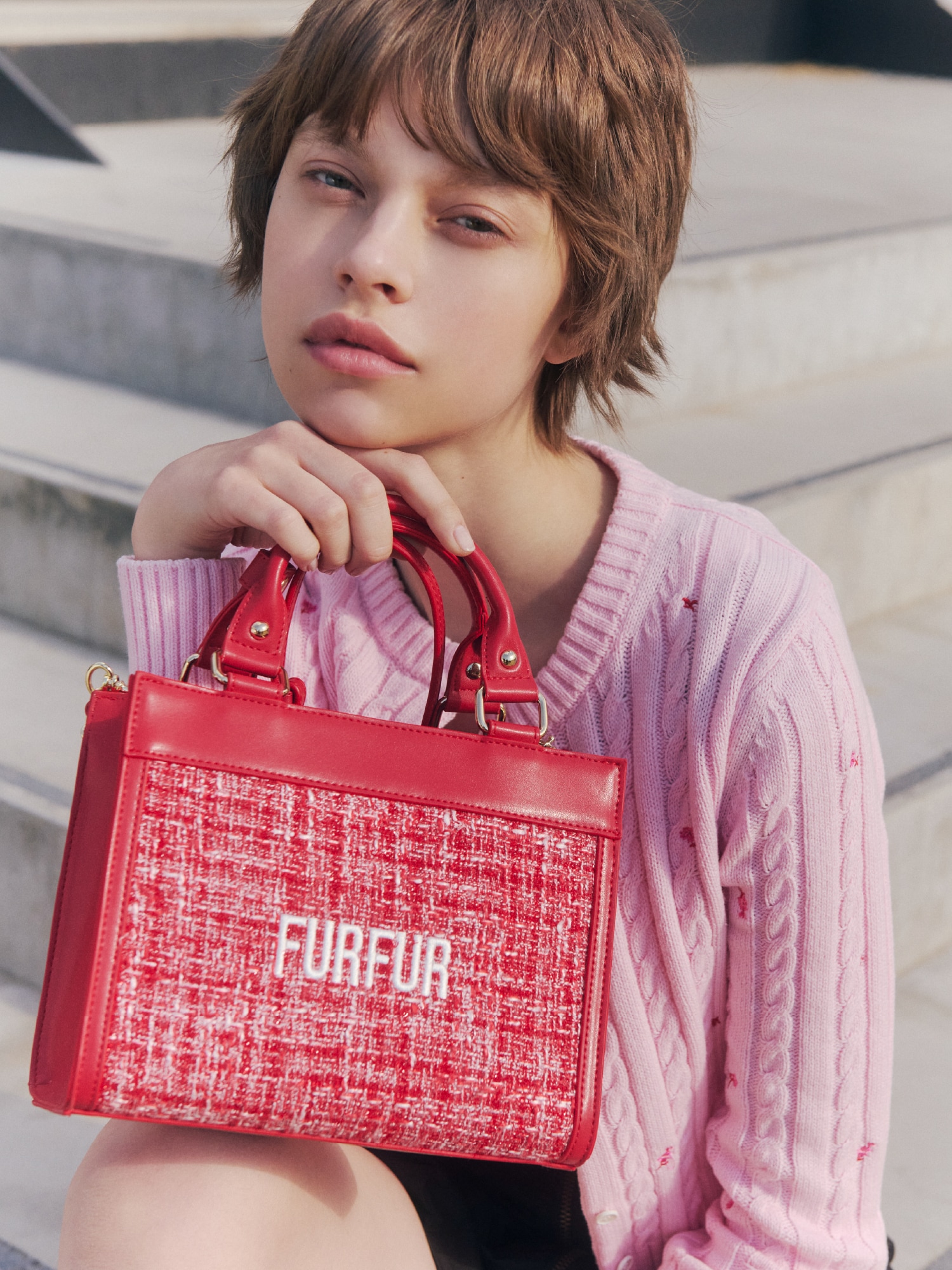 ピンクのカーディガンとピンクのビスチェにブラックのスカートを合わせ、レッドのバッグを取り入れたコーディネート。