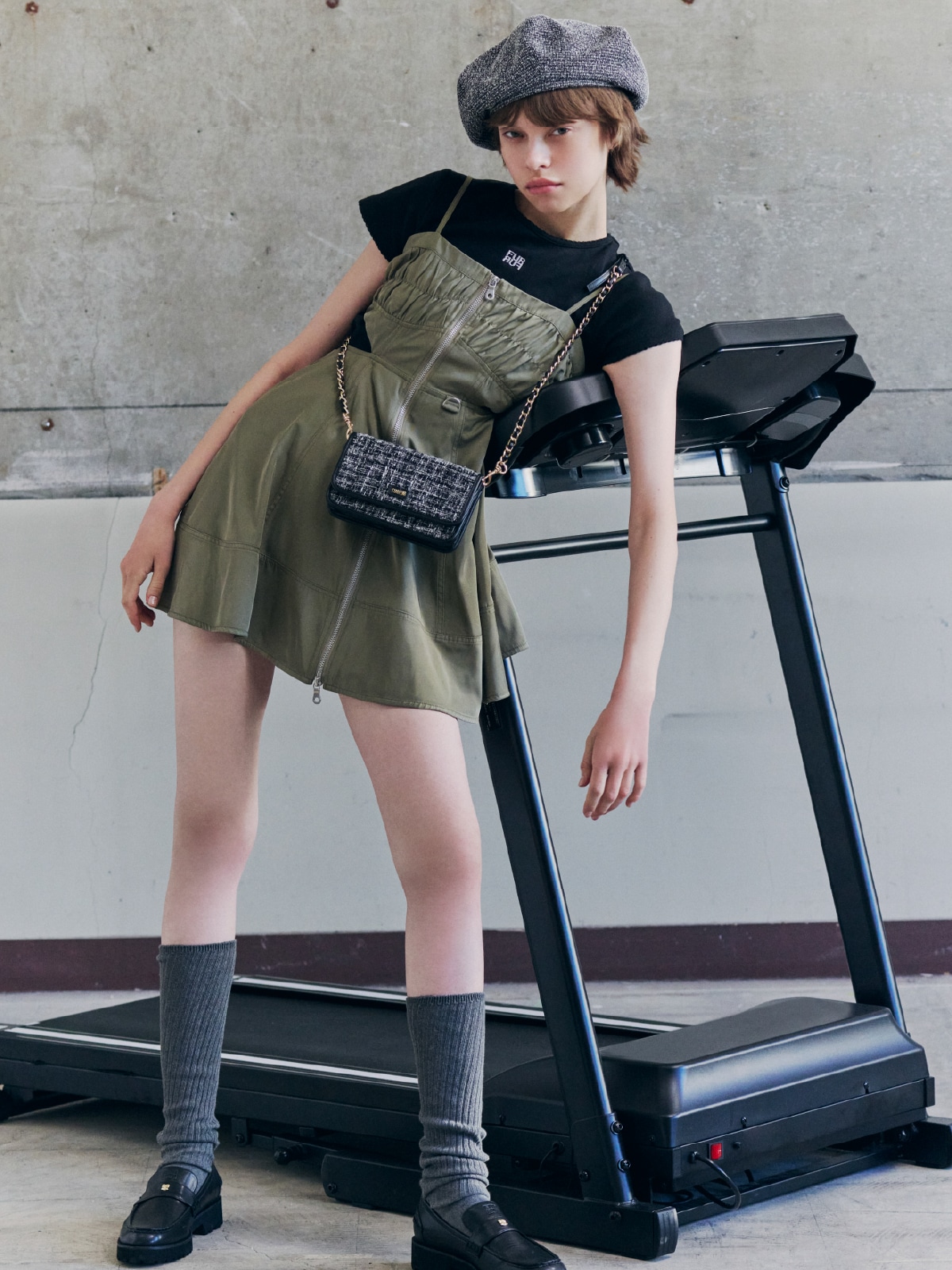 カーキのワンピースにブラックのTシャツとブラックのベレー帽、ブラックのバッグ、グレーのソックス、ブラックのシューズを合わせたコーディネート。