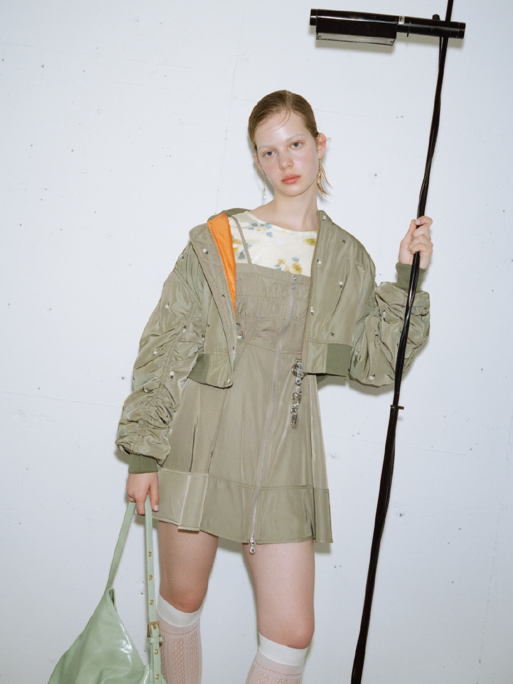 カーキのフラワー刺繍ＭＡ−１・イエローのぼかしフラワープリントシアープルオーバー・カーキのミリタリーキャミソールワンピース・白のハートモチーフイヤリング・シルバーのロゴハートバッグチャーム・ミントの２ＷＡＹソフトショルダーバッグ・ブラウンのミニリボンカシメローファーを合わせた、甘めのディテールが大人可愛いムードを添えるコーディネート