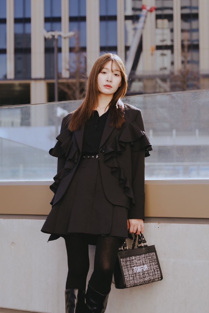 黒のツイードロゴトートバッグとフリルデザインテーラードジャケットとベルト付きタックミニスカートを合わせたコーディネート