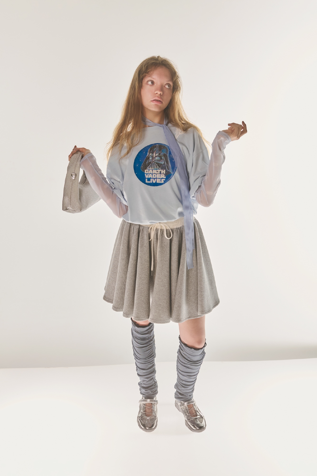 サックスのグラフィックプリントレースTシャツとロゴシアープルオーバー・グレーのミニスカート・ライトブルーのボリュームチュールドレス・イヤリング・ショルダーバッグ・トレンカ・シルバーのメリージェーンデザインスニーカーを合わせたコーディネート