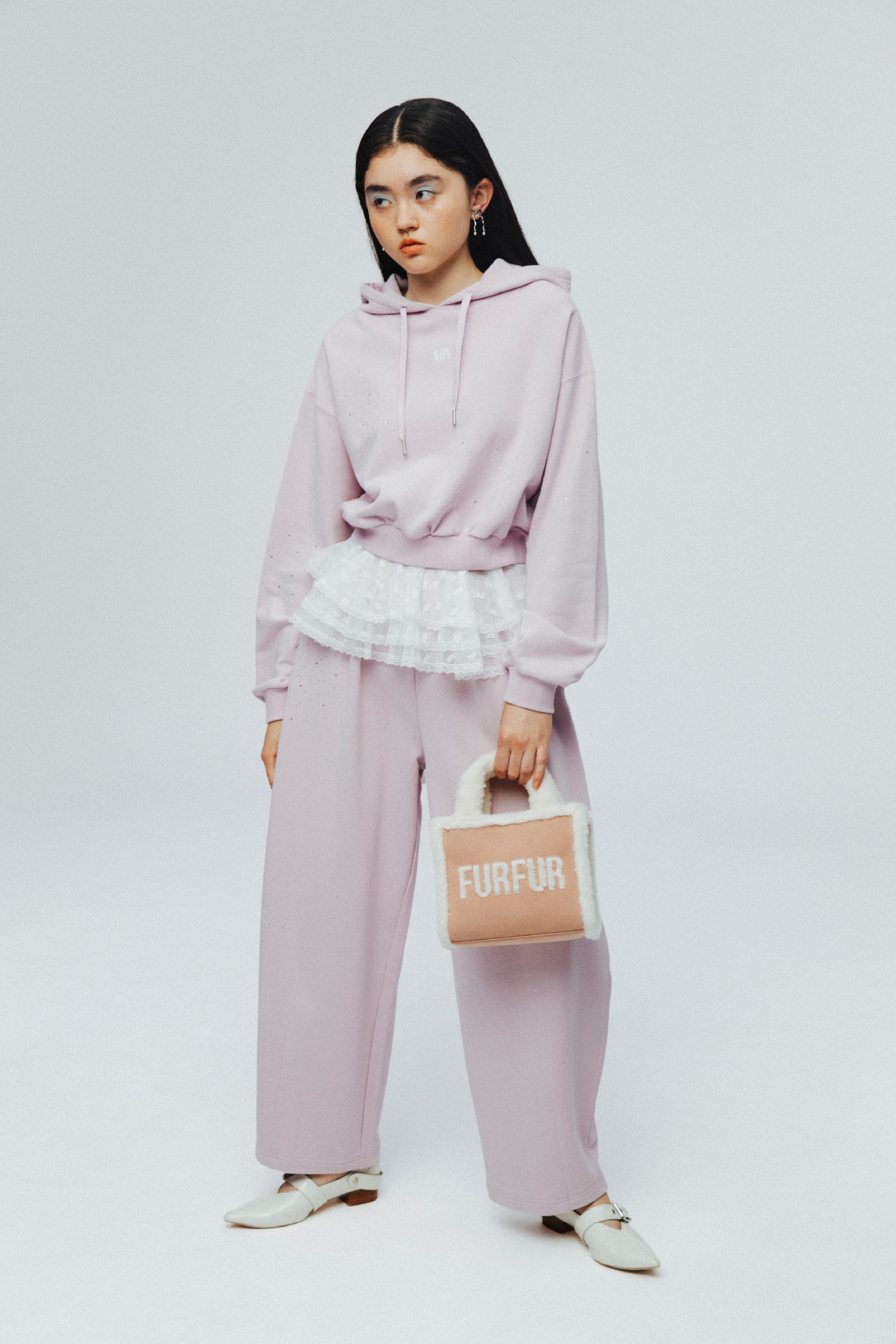 ビジュークロップドフーディー・ビジュースウェットパンツ・【WEB・一部店舗限定カラー】ムートンロゴトートバッグ・スウィングリボンイヤリング・レース付け襟・ダブルストラップバブーシュを着用した女性