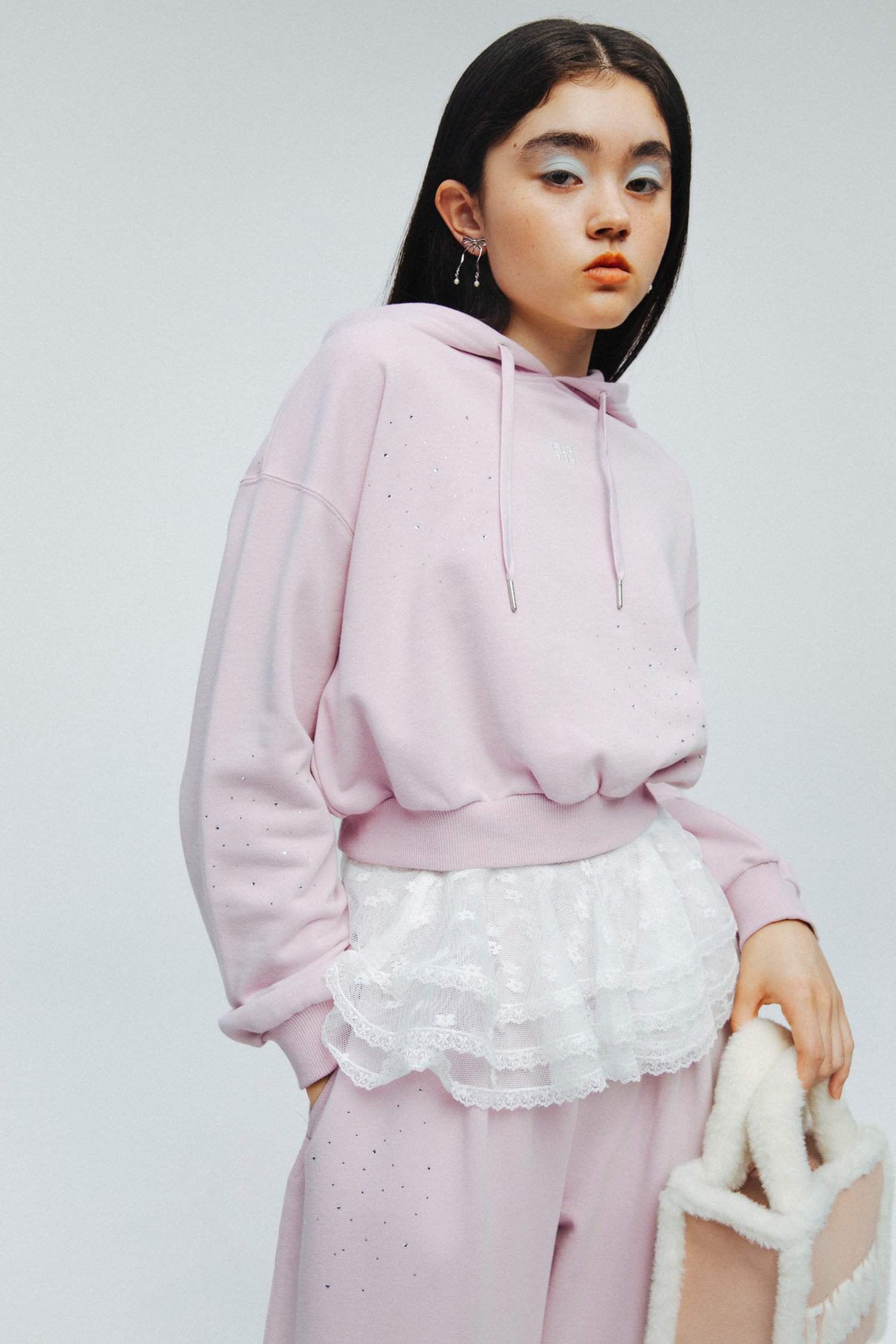 ビジュークロップドフーディー・ビジュースウェットパンツ・【WEB・一部店舗限定カラー】ムートンロゴトートバッグ・スウィングリボンイヤリング・レース付け襟・ダブルストラップバブーシュを着用した女性